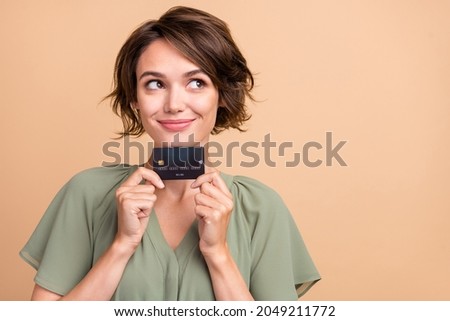 Photo of cheerful dreamy girlish lady hold debit card look empty space wear green dress isolated beige color background
