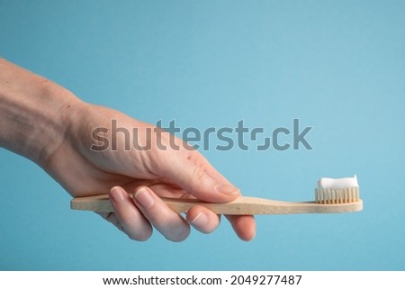Hand holding bamboo toothbrush on blue. Holding wooden eco toothbrush. Natural toothpaste on a bamboo toothbrush Royalty-Free Stock Photo #2049277487