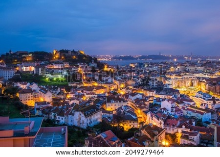 An evening scenic aerial view of the city of Lisbon illuminated by evening lights - the capital of Portugal, located on the hills and washed by the waters of the Atlantic Ocean, the Tagus River.