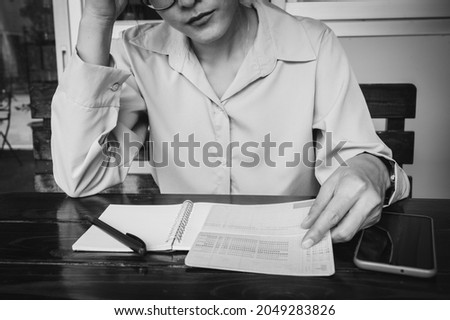 Monochrome shot of woman having stressed while looking at saving account passbook. Conceptual shot of bankrupt woman having problem of income, budget and economic crisis. Royalty-Free Stock Photo #2049283826