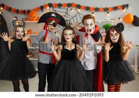 Small home party for Halloween with children in spooky costumes such asa vampire, witch and pirate. Boys and girls with scary makeup in room with holiday decorations scream and scare looking at camera