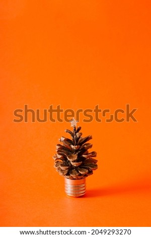 Pinecone on the part of the bulb and a star on the top on an orange background. Christmas and New Year minimal concept with large copy space