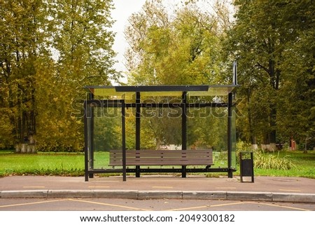 empty bus stop on an autumn day. A glass bus stop with a bench against the background of trees during the day. Stop without people. Royalty-Free Stock Photo #2049300182