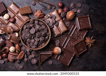 Pieces of broken tasty milk and dark chocolate bars with drops, cocoa beans and hazelnut on black meta background Royalty-Free Stock Photo #2049300533
