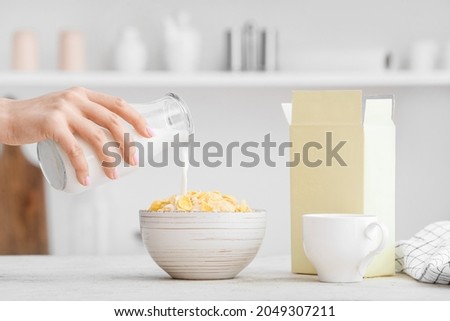 Woman pouring milk from bottle into bowl with corn flakes on table in kitchen Royalty-Free Stock Photo #2049307211