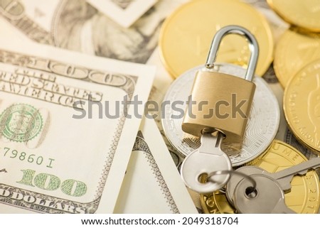 Closeup photo of golden padlock with inserted keys gold and silver coins with cryptocurrency symbols on hundred dollar bills