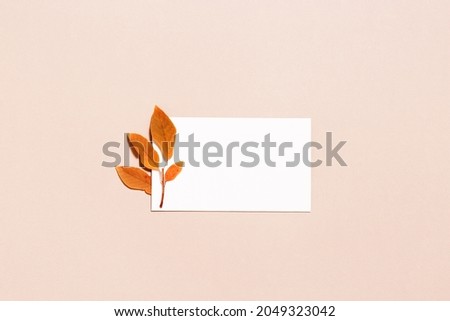 Autumn composition with empty white paper for text and red orange autumn leaves on pastel pink color background. Minimal flat lay, fall concept. Copy space