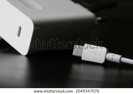 White usb type-c plug on a black background next to the white power supply and fast charger with usb type-c connector. The concept of modern technology and fast charging. Selective focusing. Macro