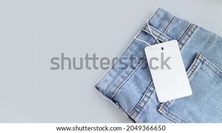 Blank white cardboard tag or label with rope on jeans clothes background