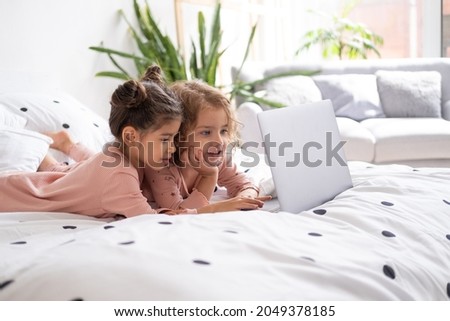 cute little kids girls in pajamas using laptop in bed at home. Kids using technology.