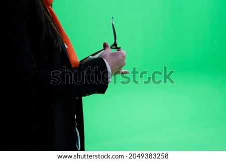 A businesswoman is holding glasses in her hand in a greenscreen studio.