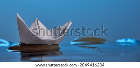Horizontal shot of paper origami boat on the stone in blue water. Photo with copy space.