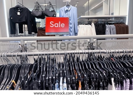 Red stand with inscription sale in white letters. Big discount price in shopping center. Advertising of Black Friday cheap clothes.Season sale concept with clothes hangers at the foreground.