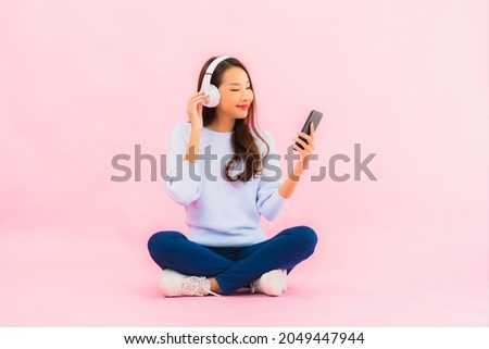 Portrait beautiful young asian woman use smart mobile phone with headphone for listen music on pink background