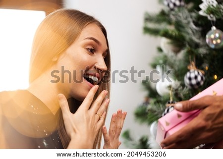Surprised young woman opens a pink box with a present .