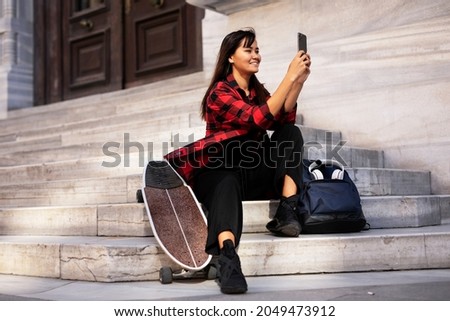 Portrait of young beautiful girl with skateboard. Happy smiling woman taking selfie photo	