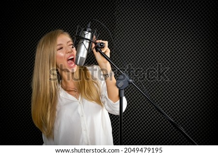 Young caucasian female singing in front of black soundproofing walls. Musicians producing music in professional recording studio.