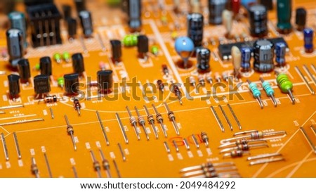 An old orange printed circuit board with multicolored electronic components, horizontally panoramic.