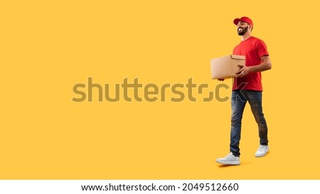 Middle-Eastern Courier Man Carrying Cardboard Box Delivering Package Looking Aside At Copy Space Posing Over Yellow Studio Background. Delivery Service. Full Length Shot Royalty-Free Stock Photo #2049512660