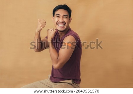 Asian man showing shoulders after getting a vaccine. Happy man showing arm with band-aids on after vaccine injection.