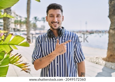 Young handsome man listening to music using headphones outdoors cheerful with a smile of face pointing with hand and finger up to the side with happy and natural expression on face 