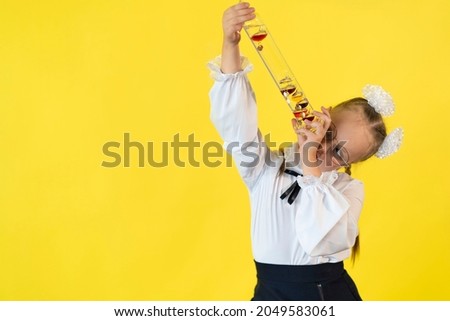 A child girl on a yellow background holds a flask with a colored liquid. Concept of science, chemistry, school