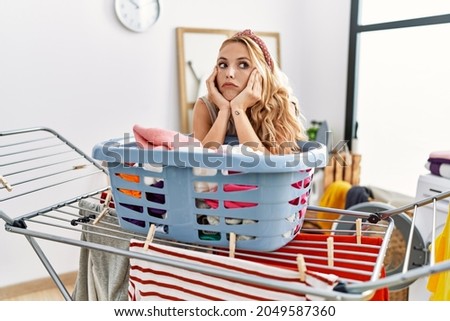 Young blonde woman boring doing laundry at laundry room