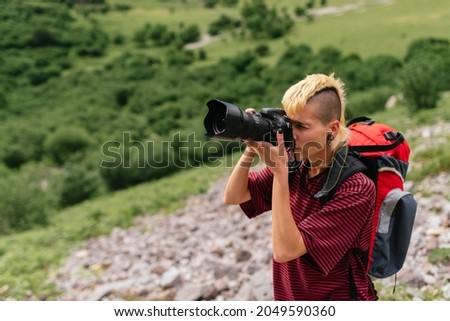 Young traveler woman with backpack taking pictures during a mountain hike.