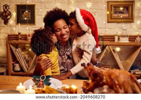 Happy African American mother enjoying while her children are kissing her at dining table for Christmas.