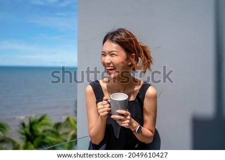 Portrait of smiling happy cheerful beautiful pretty Asian woman relaxing, drinking hot coffee or tea, standing alone outside on summer beach, Scenery Beautiful sea, candid photos, cafe, hotel.