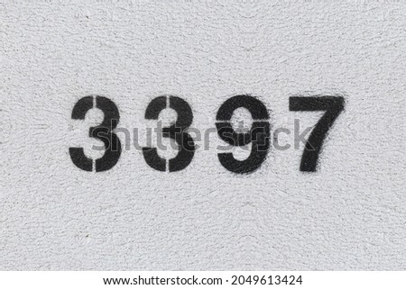 Black Number 3397 on the white wall. Spray paint. Number three thousand three hundred and ninety seven.