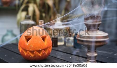 Orange pumpkin for halloween, jack-o-lantern with scary carved eyes, mouth.Candles, old lamp, spiderweb on wooden table near barn. DIY home,street decoration, entertainment for children, horror.