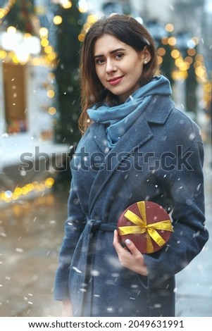Attractive brunette woman holding gift box near the christmas fair during the snowfall