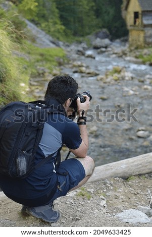 man photographs a wooden house by the river