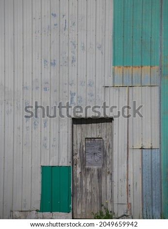 outside wooden barn door and barn wall made of tin of different colours from grey, cream to green and blue old tin barn with shapes and different colours and patterns for grunge background type room