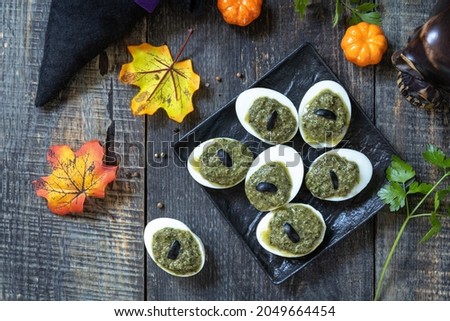 Halloween funny idea for party food. Halloween creative stuffed eggs with pesto sauce on a wooden table. Top view flat lay background.