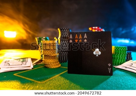Black poker cards, four aces, and stacks of colorful chips on the green poker table. Interesting lighting. No people in the picture. Gambling, gambling, poker.