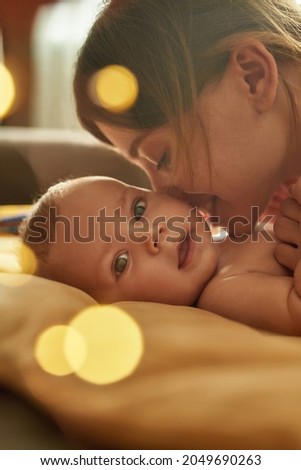 Lovely mother loves to smell her adorable baby. Sweet child lying on back, close up face. Mother leaning over her baby, sniffing its smell. Closeup portrait with bokeh balls. Royalty-Free Stock Photo #2049690263
