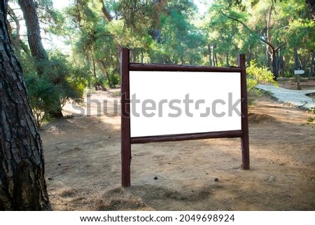 A wooden blank signboard in the green park. White, empty signboard for mock up in the forest.