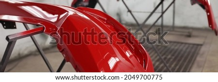 Red plastic car bumper drying after repainting in spraying booth Royalty-Free Stock Photo #2049700775