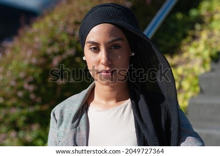 Portrait of an unsmiling muslim woman standing near park stairs looking at camera in a sunny day. Royalty-Free Stock Photo #2049727364