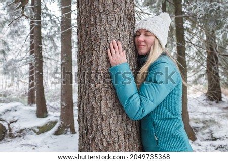 Young woman in forest on winter day. Hiker hugging tree trunk. Save of nature and the planet.