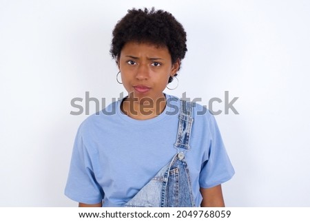 African American woman with afro hair style wearing denim overall against white wall Pointing down with fingers showing advertisement, surprised face and open mouth