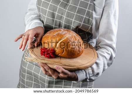 A young woman holds bread in her hands. The cook carries freshly baked bread on a tray.