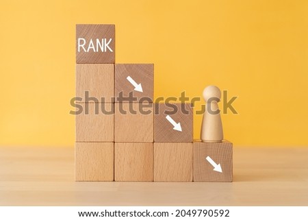 Rank down; Wooden blocks with "RANK" text of concept and a human toy. Royalty-Free Stock Photo #2049790592