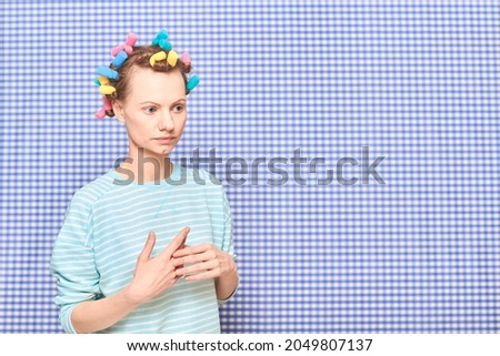Portrait of thoughtful young woman without makeup with colorful hair curlers on head, looking melancholic and dreamy, standing over shower curtain background, with place for your text and design Royalty-Free Stock Photo #2049807137