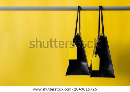 Black shopping bags with blank yellow price tags hanging on cloth rack with yellow background for Black Friday shopping sale concept.