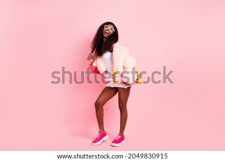 Full body photo of happy nice dark skin lady look empty space hold skate isolated on pastel pink color background