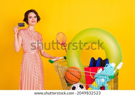 Photo of cheerful client girl carry shop cart hold credit card wear striped dress isolated yellow color background