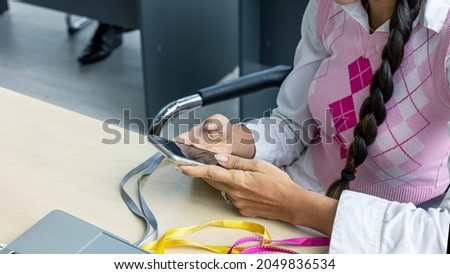 An attractive female office worker is using a smartphone to check business and market information online. Business woman use digital device to chat with customers to enhance her marketing and selling.